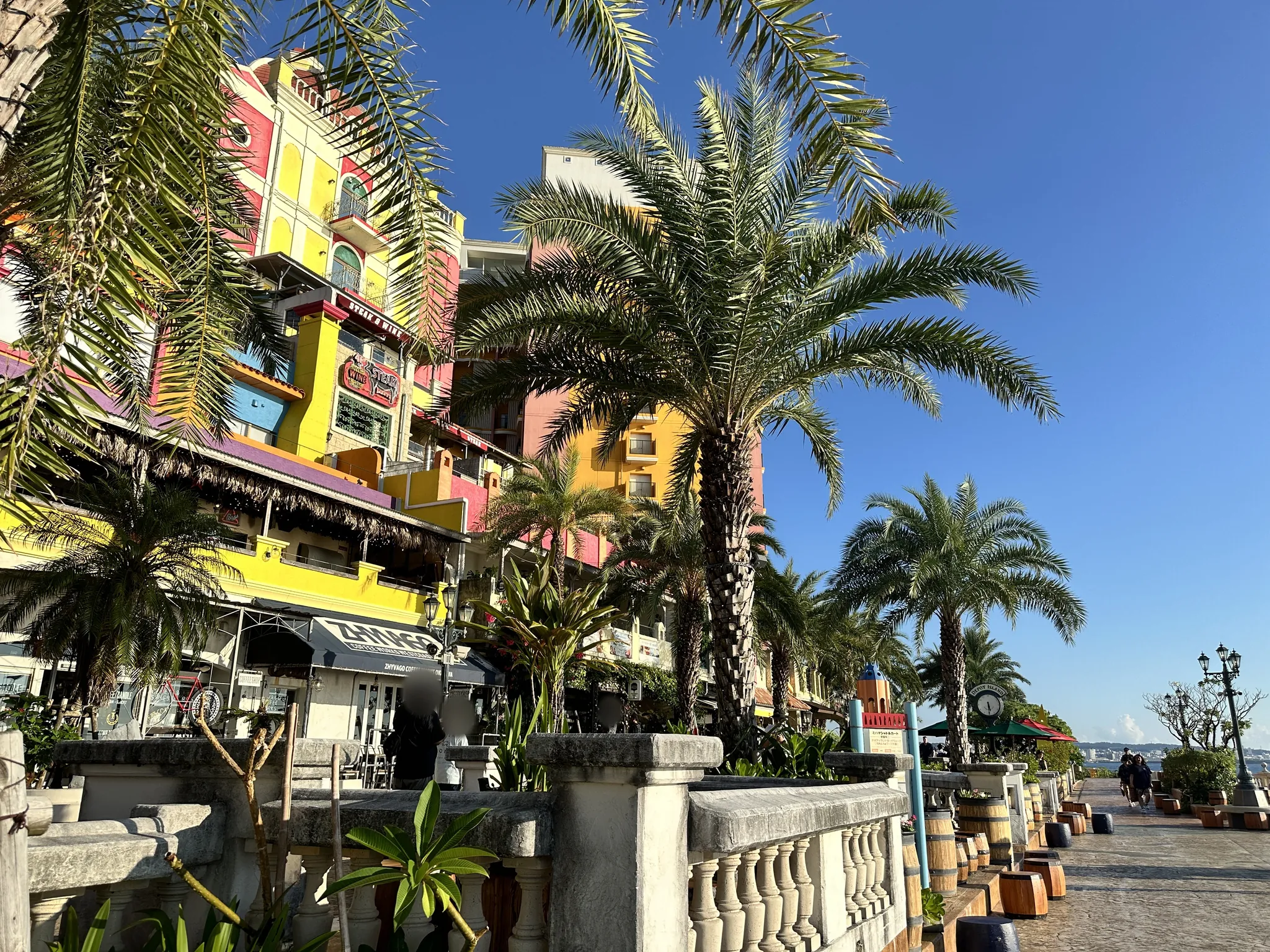Palm trees and brightly painted buildings along the seafront promenade at Mihama American Village