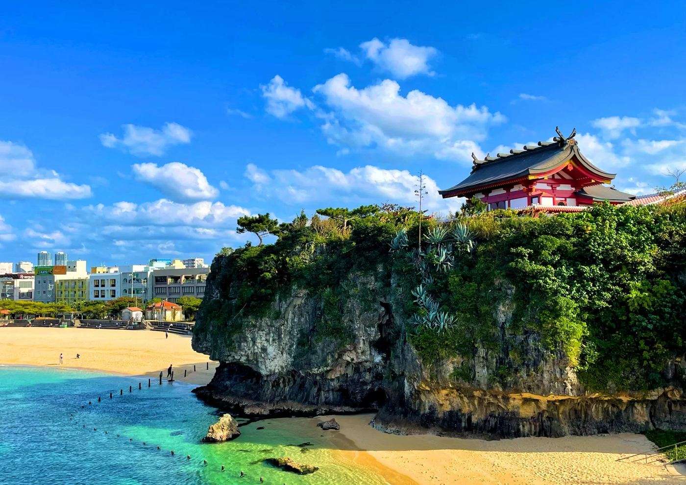 波の上ビーチの砂浜と、崖の上に建つ波上宮の朱塗りの社殿
