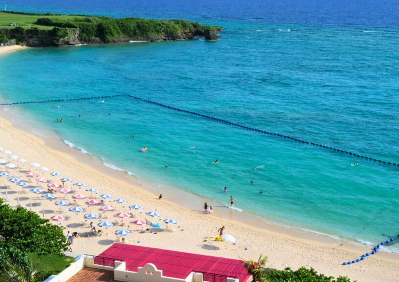 ニライビーチの弓なりの浜とターコイズブルーの海、並ぶパラソル