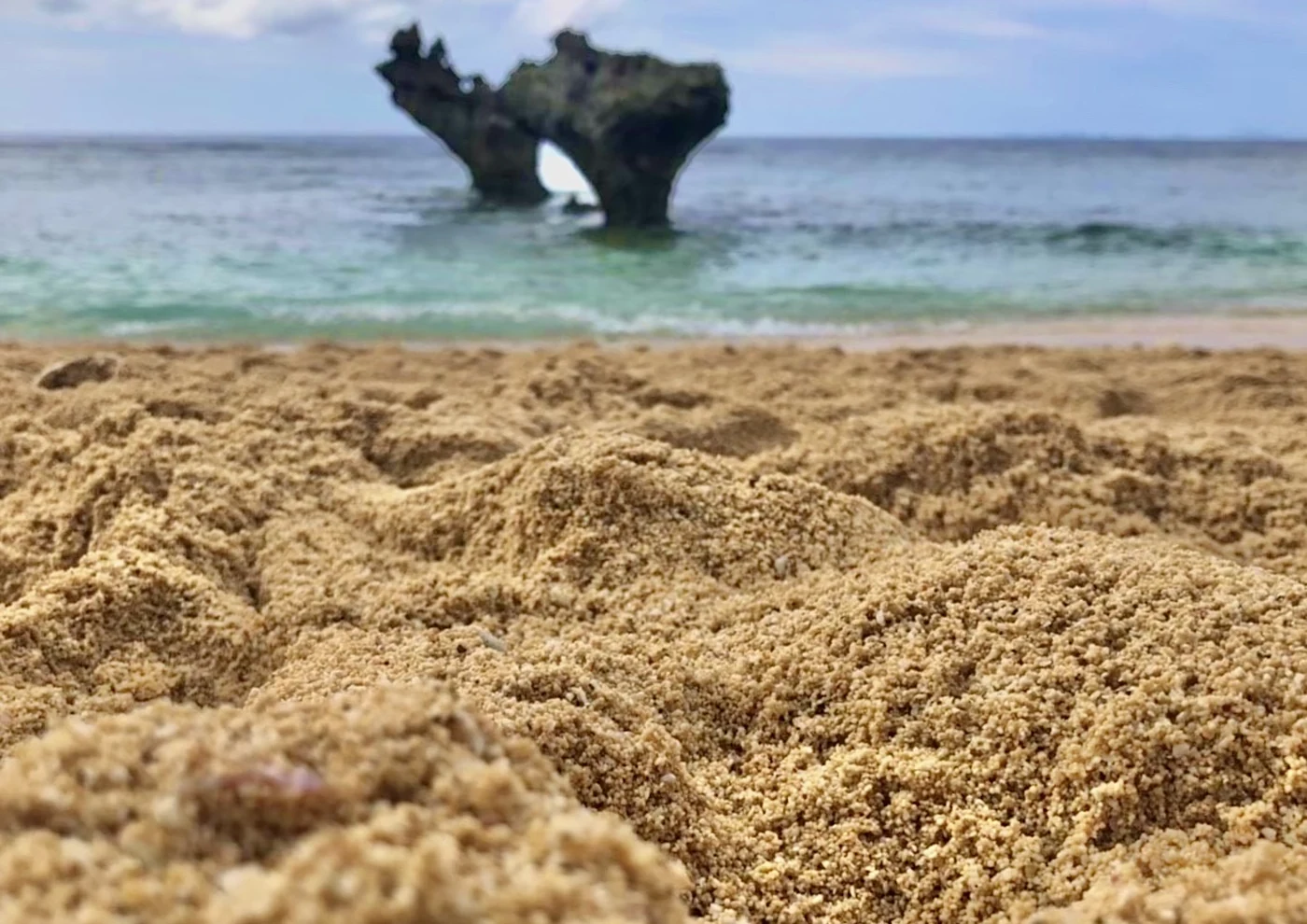 ティーヌ浜の砂と、その奥に穴のあいた岩が海に立っている