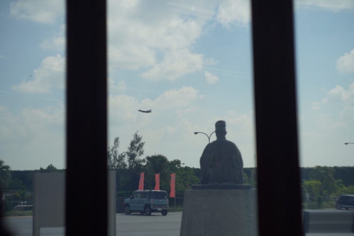 道の駅かでなの野國總管の銅像のシルエットと、空を横切る航空機