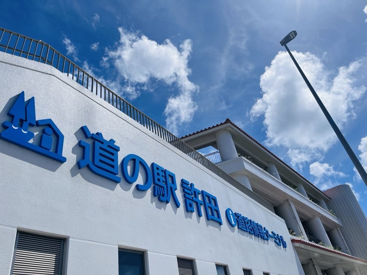 青空に立つ道の駅許田の建物と、青い立体文字の看板