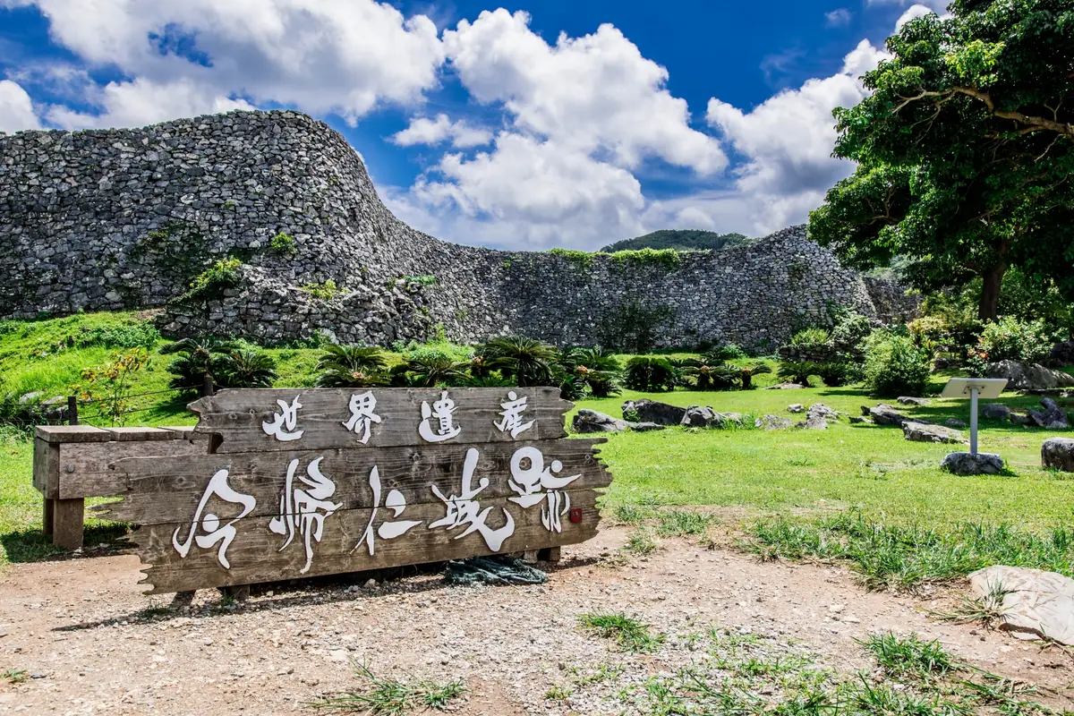 「世界遺産 今帰仁城跡」と刻まれた木の看板と、その奥のうねる城壁